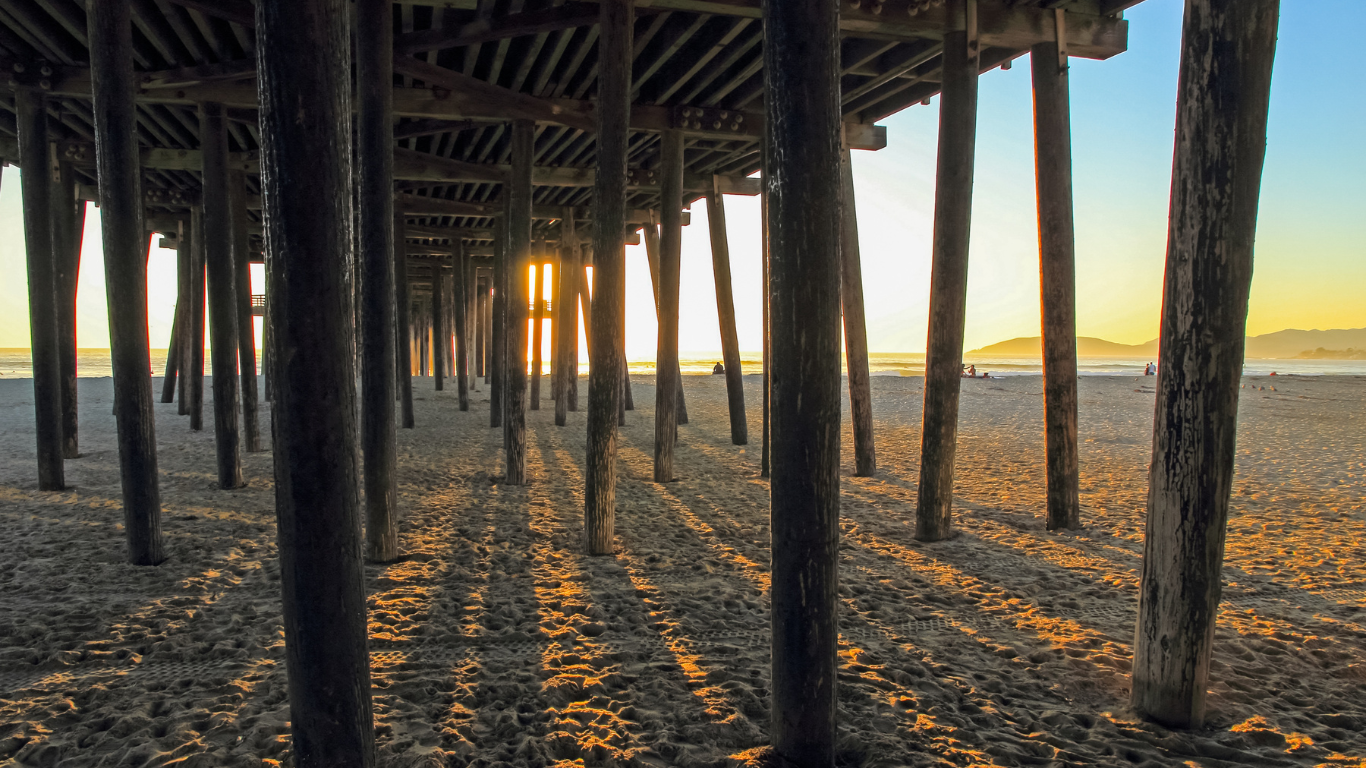 Photo taken under the Pismo Beach Pier, looking out towards the ocean, and pier pilings at near sunset. 